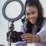 happy young black woman setting up smartphone before shooting podcast